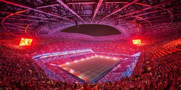 Packed Moroccan stadium at night ahead of AFCON 2025, with fans waving African flags under bright floodlights.