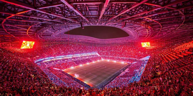 Packed Moroccan stadium at night ahead of AFCON 2025, with fans waving African flags under bright floodlights.